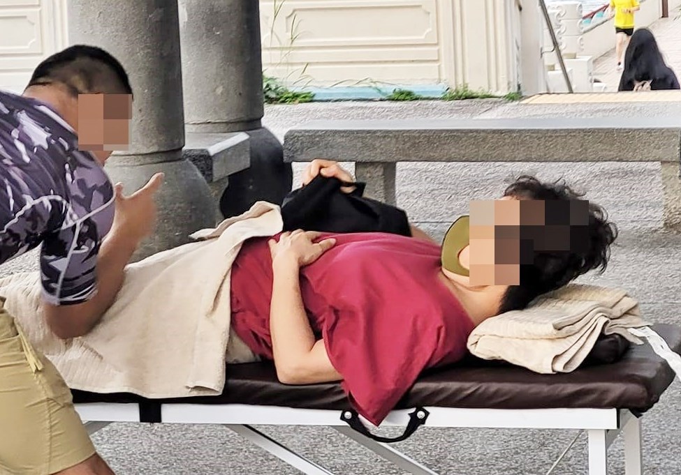 摺叠床上躺平著的红衣女子正低头探看短裤男的一举一动。网上截图
