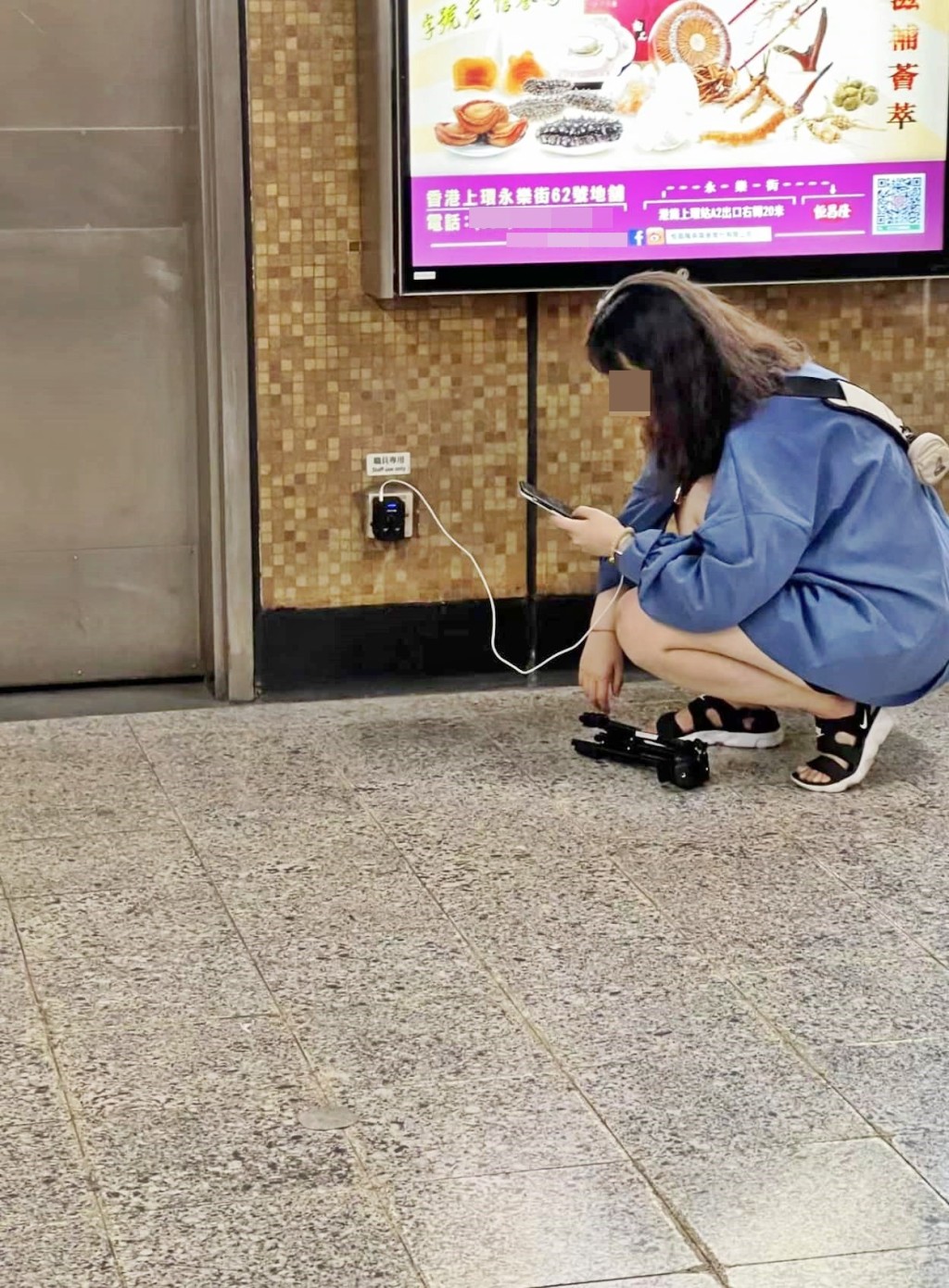 女子在叉电期间，蹲在地上全神贯注滑手机，并将随身携带的脚架放于地上。网图