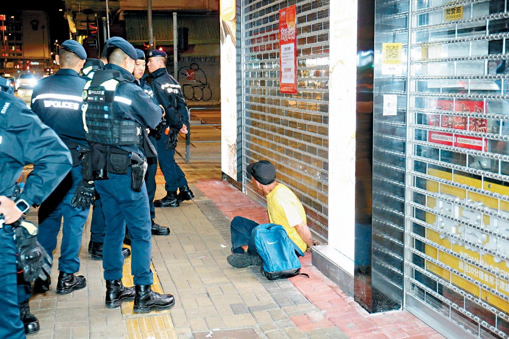 被捕疑犯雙手被手銬反鎖,盤膝坐在地上。下圖頭部受傷事主由救護車送院治理。