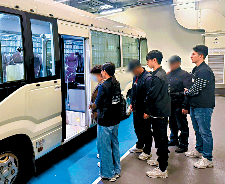 入境處人員將在反黑工行動中被捕的懷疑非法勞工押走。