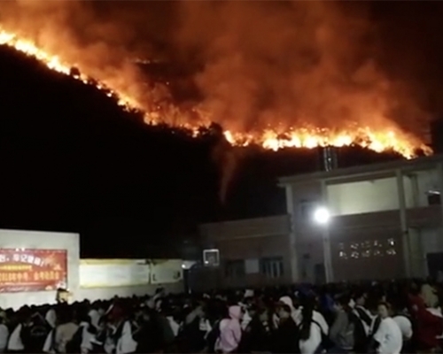 學校後山熊熊大火，山下學校仍淡定開中考動員會。（網圖）