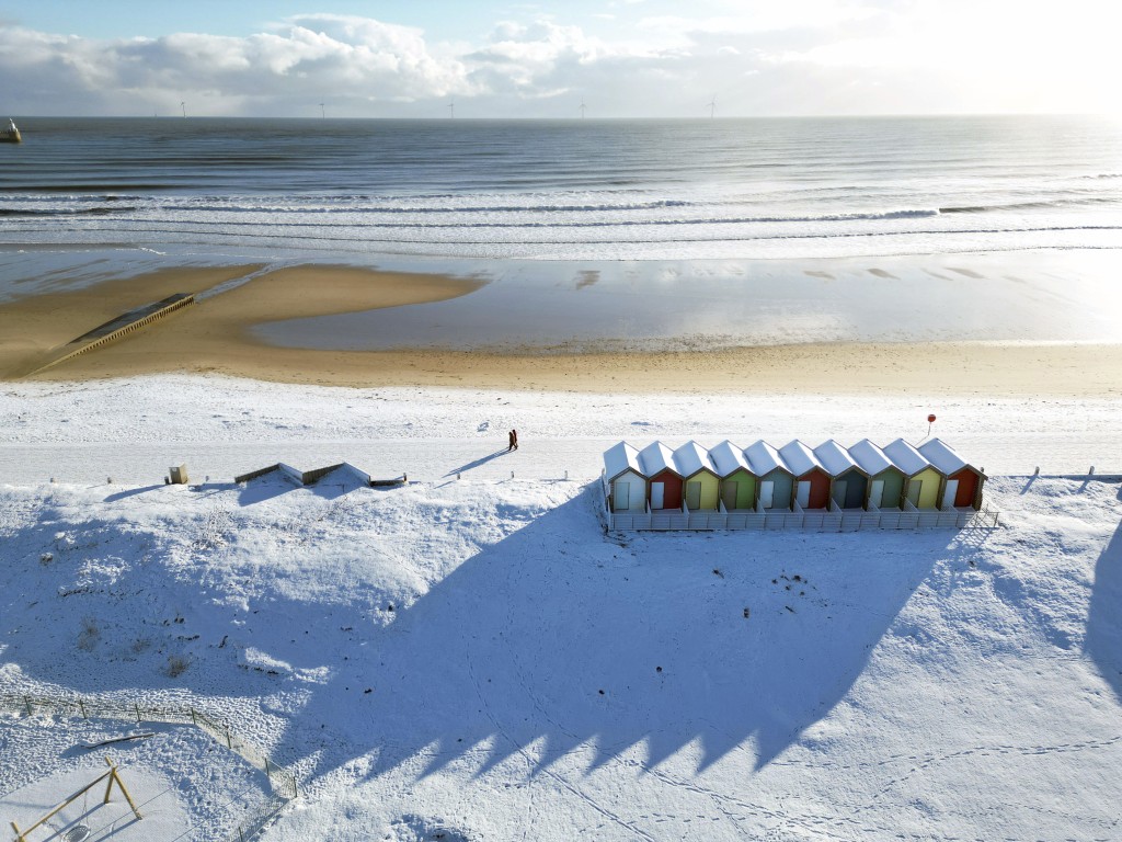 民眾在英格蘭東北部布萊斯的海灘小屋旁的雪地裡遛狗。AP