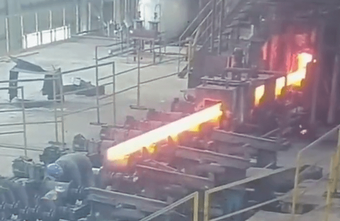 工人身後一根燒得火紅的鋼條產出，愈來愈接近。