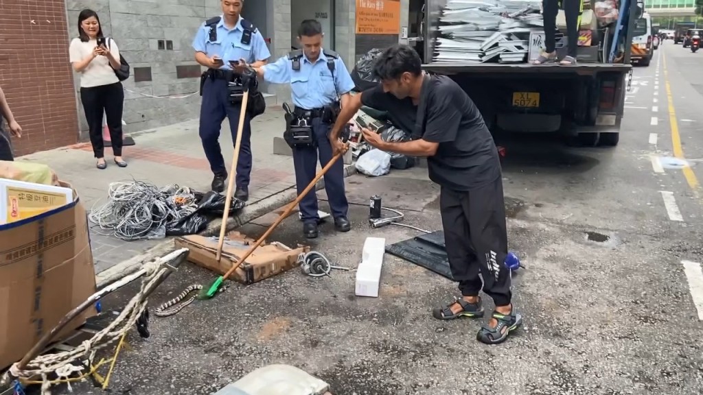 警员及一名非华裔男子用扫帚及木棍压住蛇身限制其行动。网上片段截图