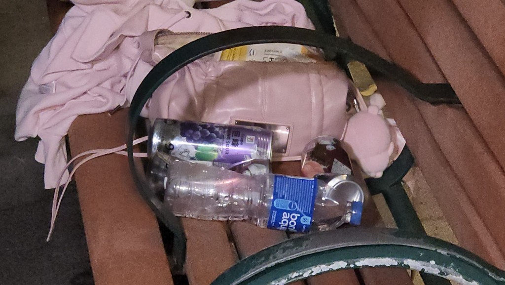 海旁長櫈上遺下疑屬女事主的物品，包括粉紅色手袋、外套、環保袋，以及兩罐果汁啤酒和一瓶飲用至一半的樽裝水，地上亦有壓扁的啤酒罐。黎志偉攝