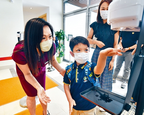 劉平齋國際學校昨舉行小一迎新日,校長許陳幹華(左)在校門迎接返校學生,並教他們如何消毒雙手。