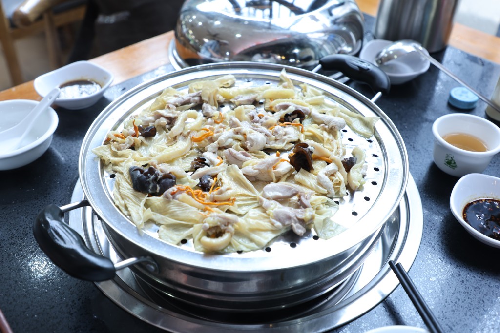 先來將雞肉放在蒸架上層蒸煮，吃來雞肉鮮嫩而且原汁原味，肉汁流向下層，搭配藥材、蔬菜等，成為由雞汁及藥材精華合成的鮮濃雞湯