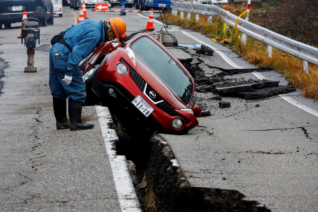 日本穴水附近，一名工人正在查看地震后陷在破损道路上的汽车。路透社