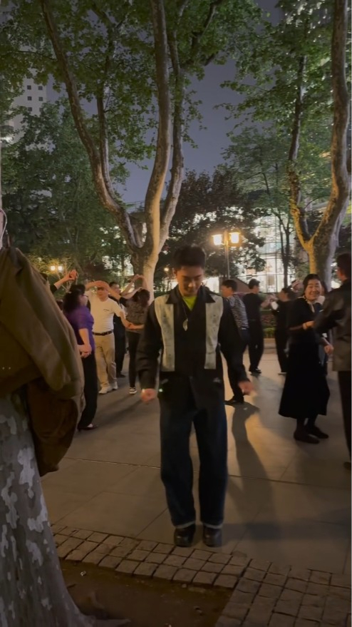 孔德贤与拍摄者到一个公园内，身旁都是中老年人，个个一双一对跳舞，而孔德贤则一个人在镜头前小幅度地摇动身躯。