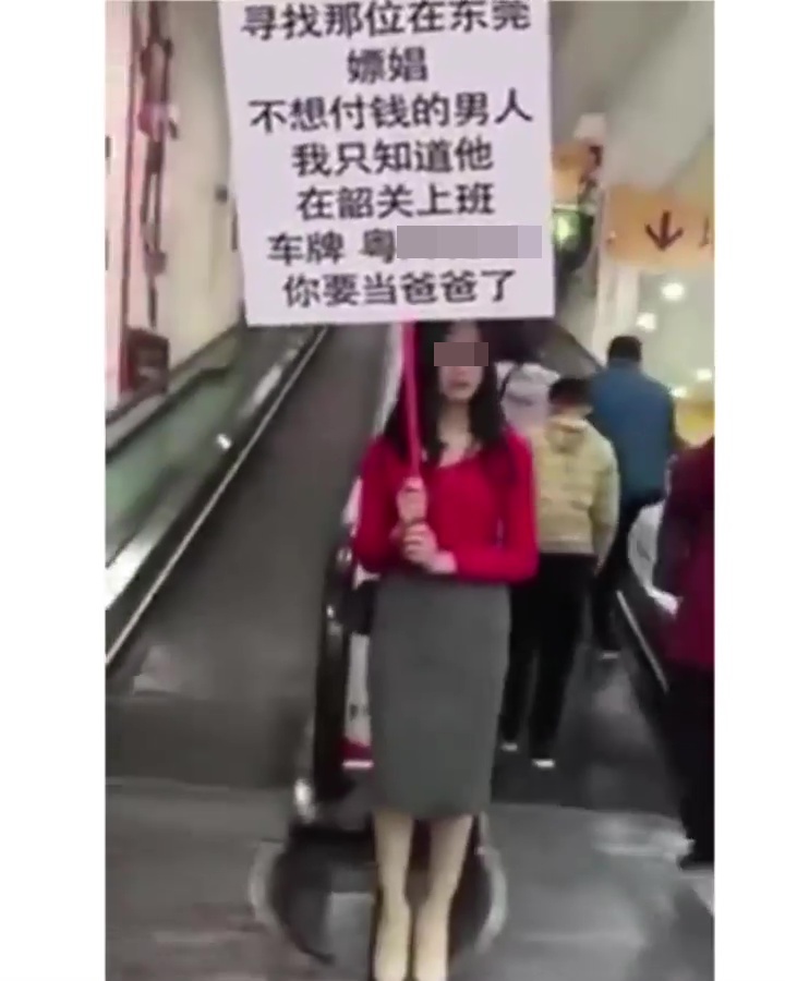 女子在连接地下停车场的扶手电梯旁，举起白底黑字的告示牌。网上截图