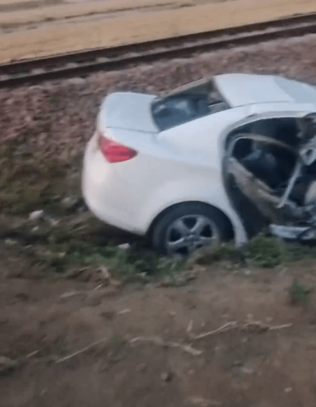 白色私家车追尾火车后，被撞倒在路轨附近。