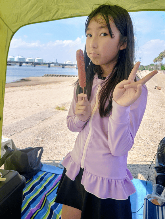 平田琉七在海灘帳篷拿著熱狗嘟嘴比V，俏皮可愛。