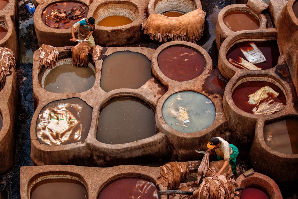 兩位工人在染缸中工作，用刀割去皮 革上多餘的部份，拍攝時以左上和右下的工人作對角構圖。