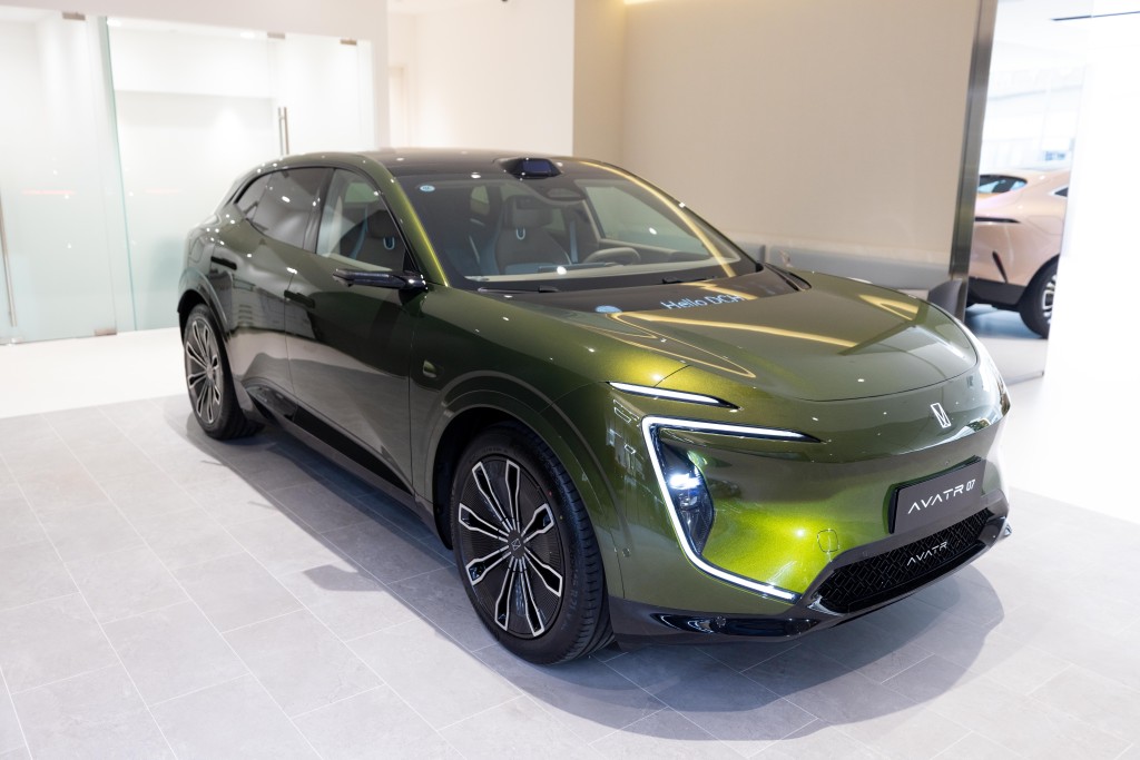 A sleek, green electric SUV with a modern front design featuring sharp LED headlights, a prominent grille, and a spacious interior with three screens visible through the windshield.