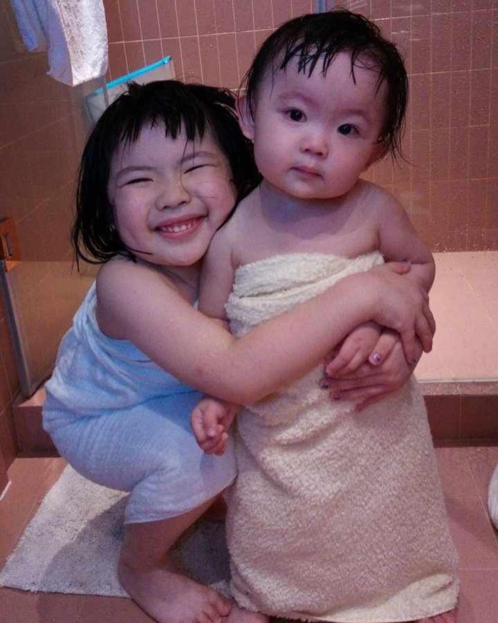 当妈妈为她们围上浴巾时，Lucy更蹲下揽住妹妹，尽显好家姐风范。