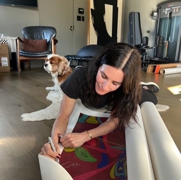 卻妮高絲在愛犬陪伴下,密密在慈善畫作上簽名。 卻妮高絲在愛犬陪伴下,密密在慈善畫作上簽名。