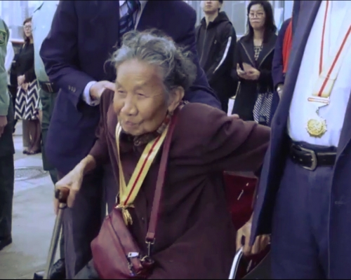 宣傳片中坐輪椅的婆婆，聽國歌時肅立。國歌快閃片段截圖