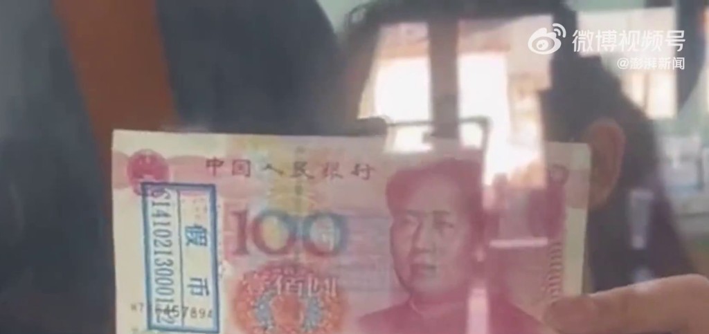 銀行櫃員舉起一張100元人民幣，紙幣被蓋上「假幣」。