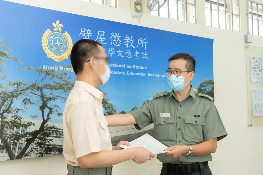 壁屋惩教所监督余学明（右）颁发香港中学文凭考试成绩通知书予青少年在囚人士小杰（化名）。