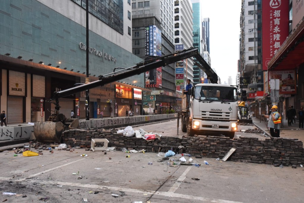 夾斗車清理馬路上堆砌的矮磚牆。