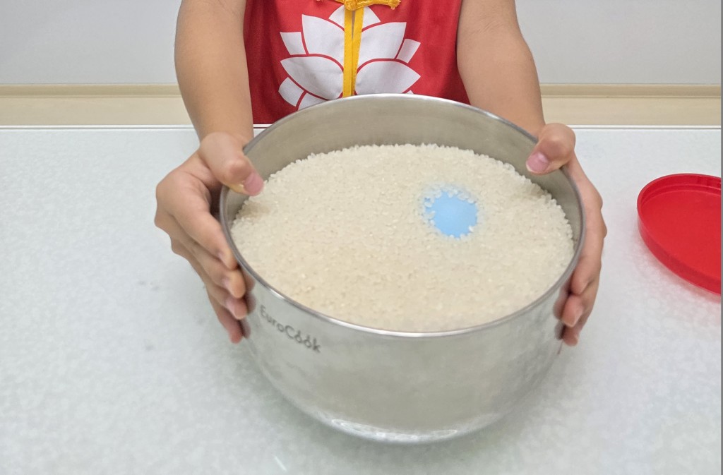 步驟3：用雙手奮力地搖晃米盆。當你看見米盆中有點顏色冒起時，請繼續搖晃，乒乓球就快要跳出來了。  *小貼士：搖晃的重點在於速度而不是幅度，小幅度及快速地搖效果更佳。（圖片來源：工程師媽媽）