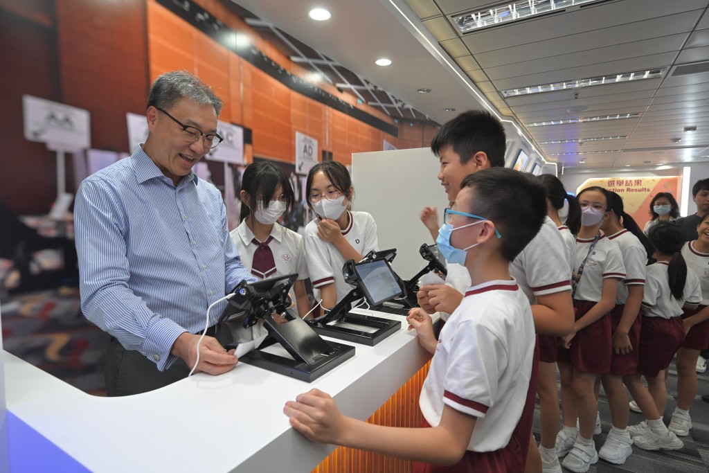 陆启康（左一）在模拟投票区，以最近几场公共选举开始使用的电子选民登记册系统向学生发出选票。政府新闻处图片