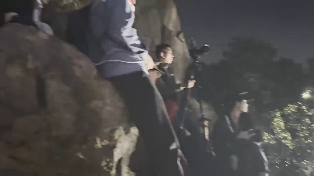 十多名男女「登顶」危坐于山坡顶岩石边缘准备睇烟花，警方要求各人返回地面。