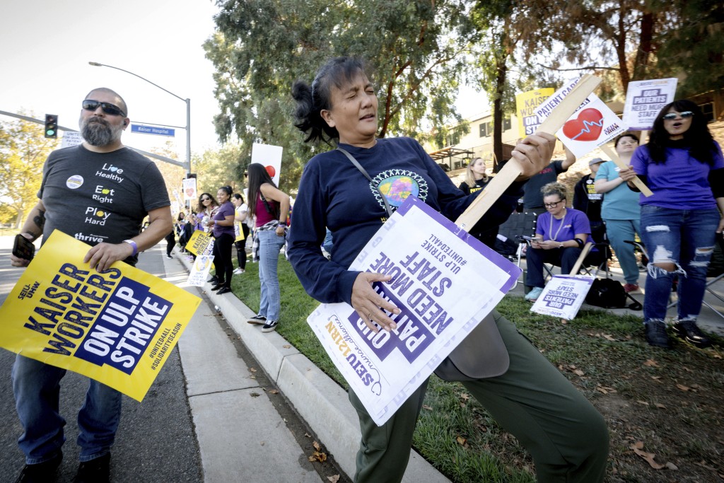 在加州莫雷诺谷举行的全国性罢工期间，有护士在凯撒医疗机构医院外示威，拿起像弹吉他一样的标语。AP