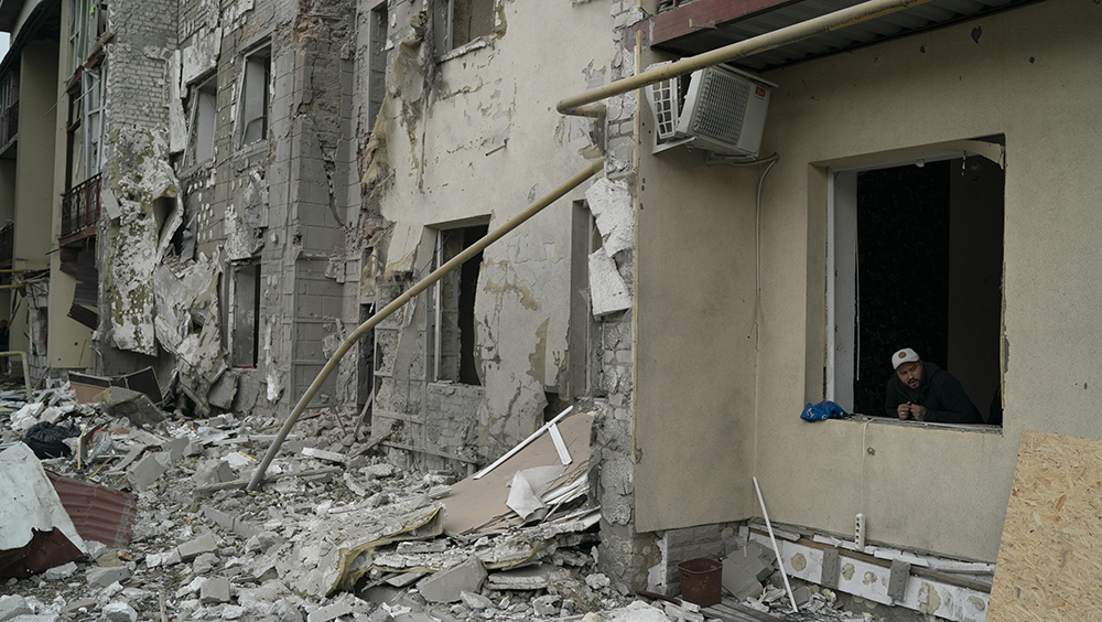 俄軍在哈爾科夫發動襲擊後，一名男子從一棟住宅樓的窗戶向外望去。AP