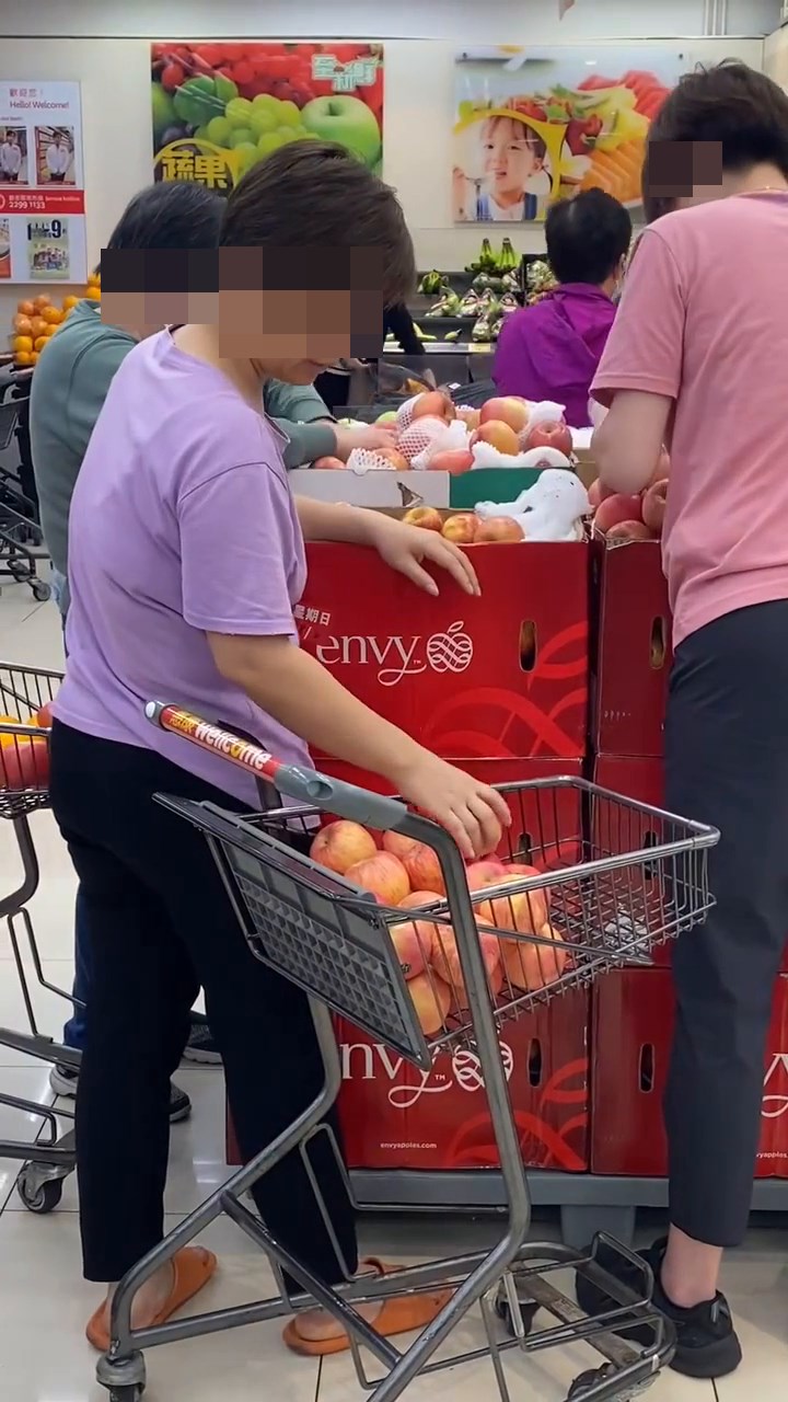大媽以極小心的輕輕手將蘋果安放購物車內。網上短片截圖