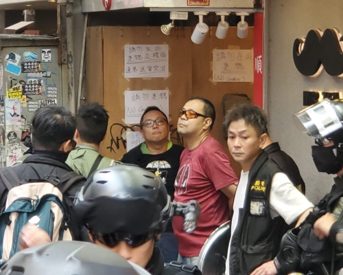 譚得志（戴眼鏡黑衣）被警方帶走。