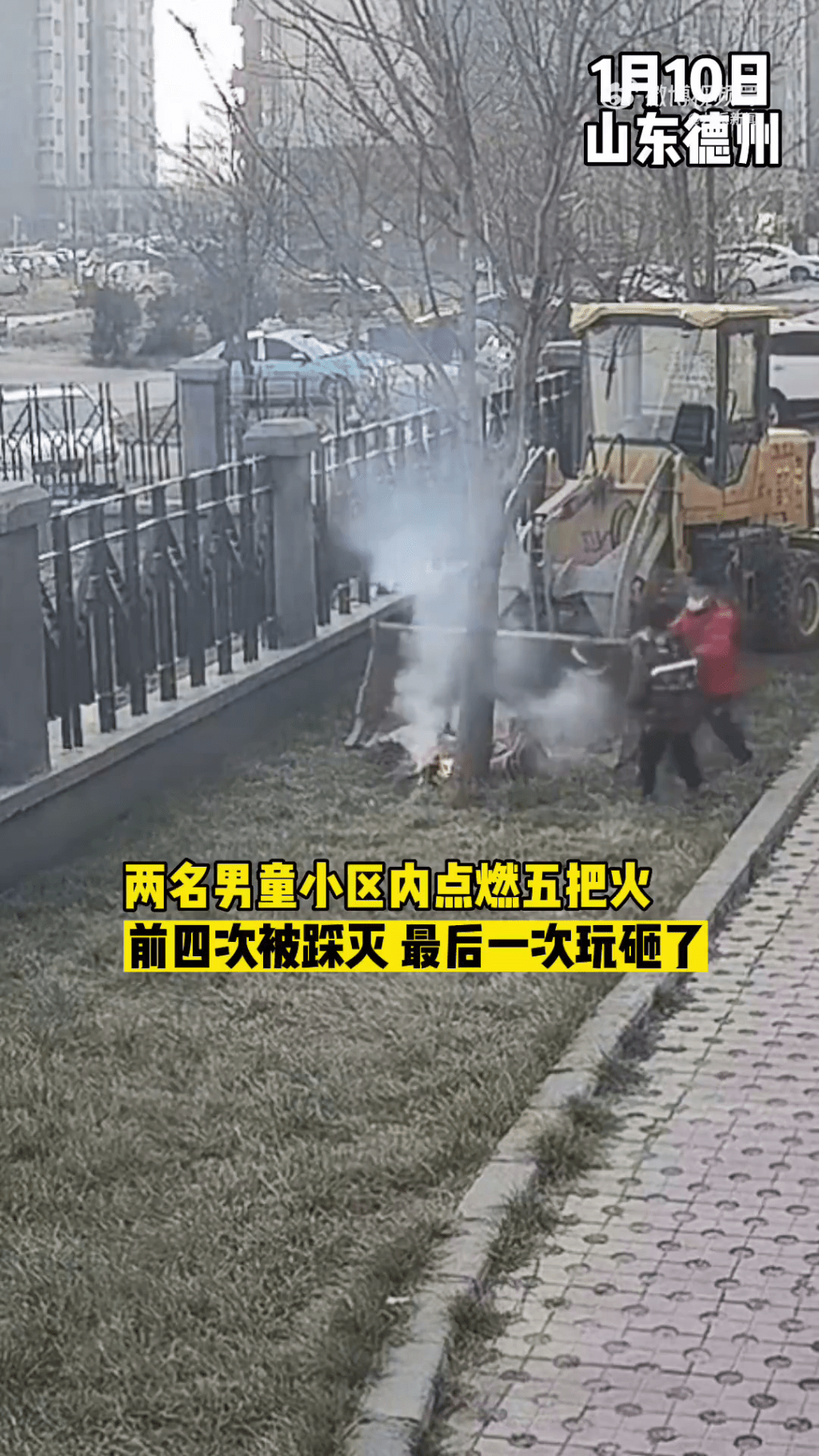 两名小童在社区一辆铲车后玩火，杂草被烧得冒出白烟。