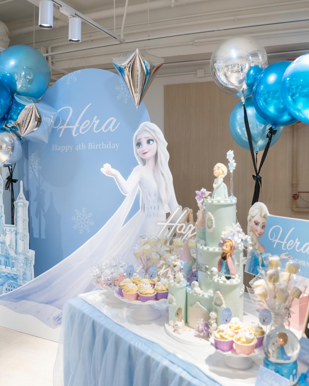 现场配合主题《冰雪奇缘》以粉蓝及银色的气球布置，布景板写上“Hera Happy 4th Birthday”。