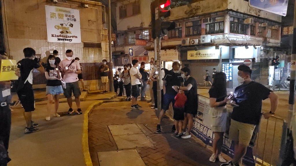 未能進入教堂內的市民在路口開著手機燈光悼念。