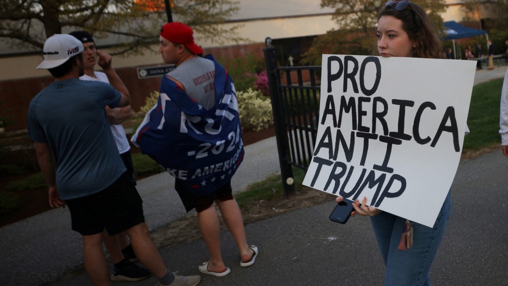 示威者持标语牌从特朗普支持者身后走过。 路透社