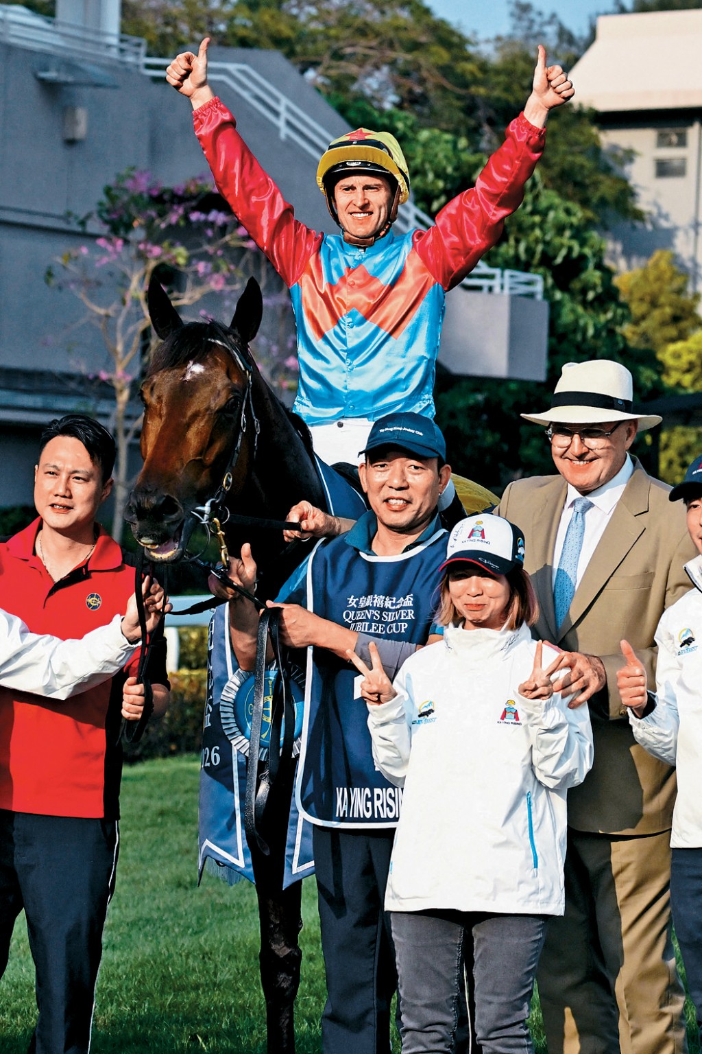 「嘉應高昇」騎師潘頓勝後，與練馬師希斯及工作人員合照時，舉手示勝。