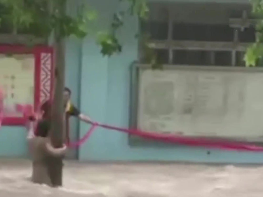 路人用廣告條幅營救被困洪水的女子。網圖