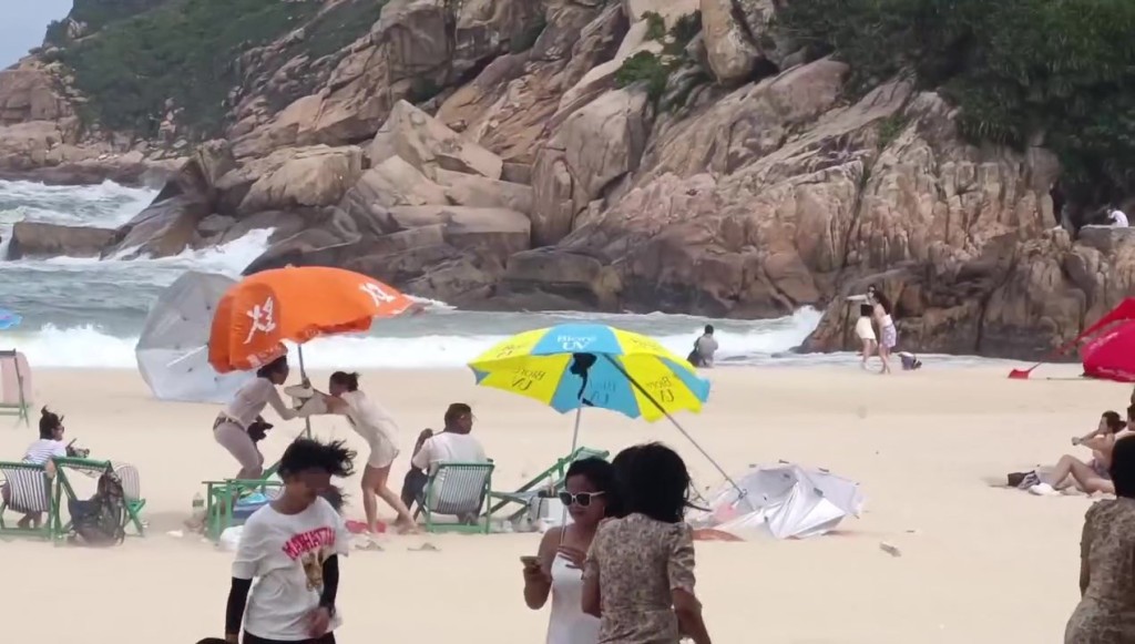 有泳客拉著太陽傘與強風搏鬥。網上截圖