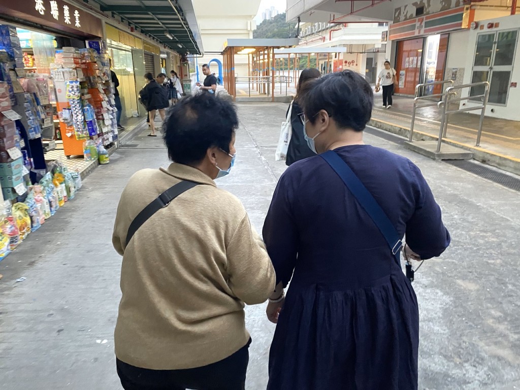 在邨内居住40年的旧街坊李女士(左)，带着新入伙、撑拐杖行动不便的陈女士视察邨内环境。(源琛薇摄)