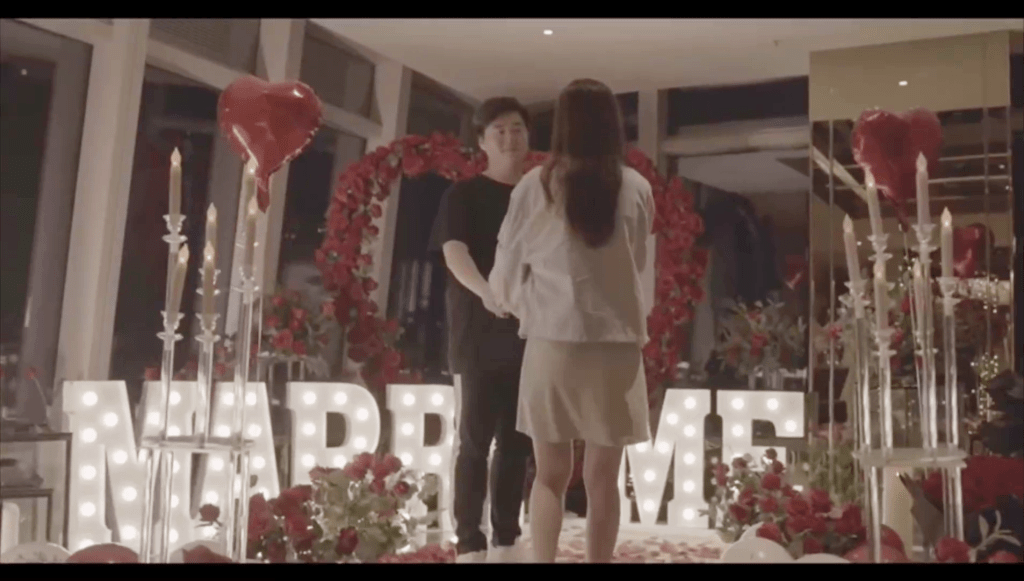 Calvin站在約兩尺高的「MARRY ME」字形燈，以及鮮花堆砌的巨型心心前，向陳嘉慧單膝下跪求婚。