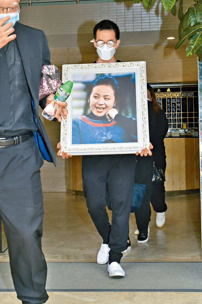 兒子捧着謝月美遺照步出靈堂。