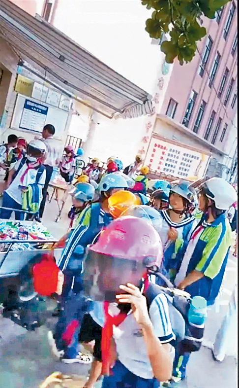 佩戴头盔的学生走出校门。