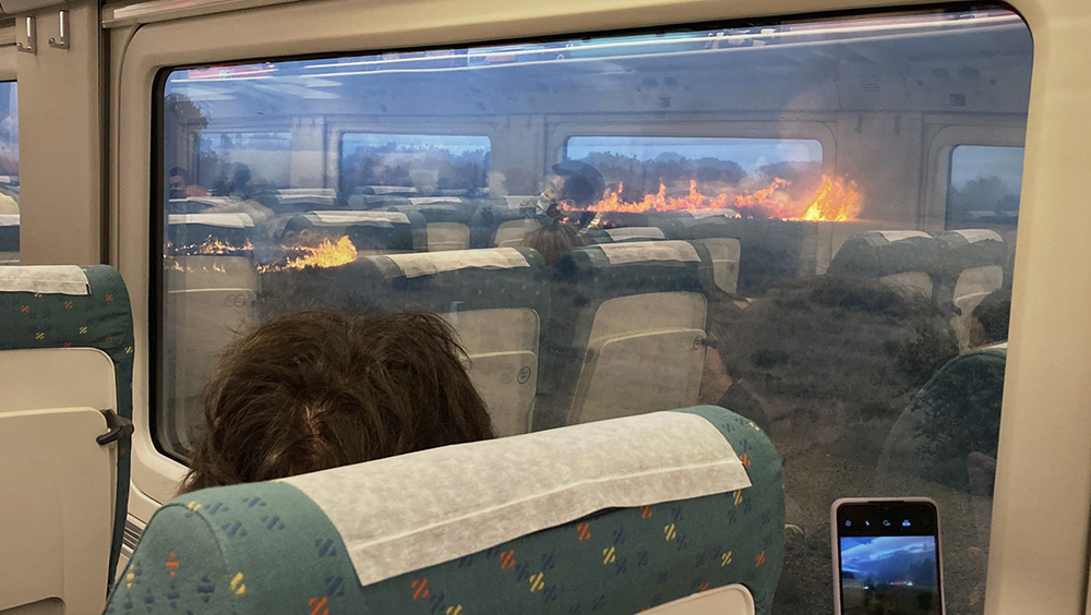 乘客在停滯的列車窗外兩側看着火焰衝天的山火感到不知所措。網圖