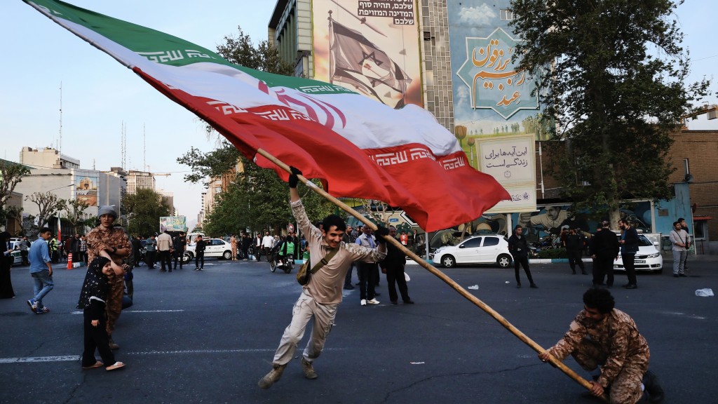 伊斯兰革命卫队攻击以色列后，人们上街庆祝，在巨型反以壁画旁挥舞伊朗国旗。路透社