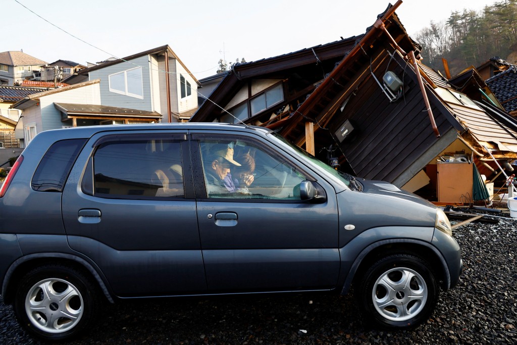 日本石川縣輪島，地震後住在車裡的一對夫妻在被毀壞的房子前在車裡吃早餐。 路透社