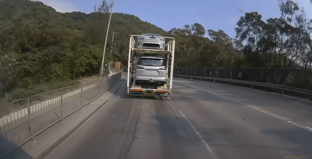 網上瘋傳一段車Cam片段，顯示今日（9日）下午約4時許，一輛載有兩部私家車的雙層運輸車，行經青衣西草灣道、近九巴車廠對開時發生罕見事故。