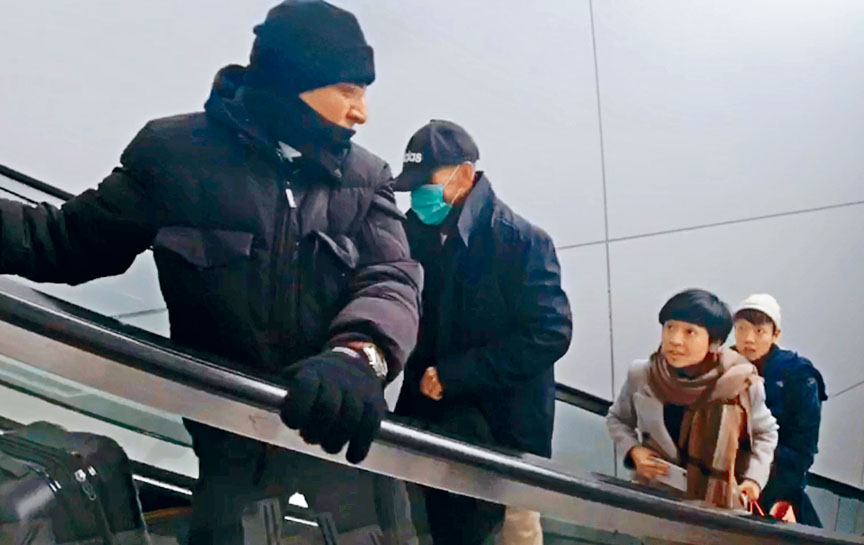 ■接機男子一前一後，帶着季炳雄(左二)乘扶手電梯前往停車場。