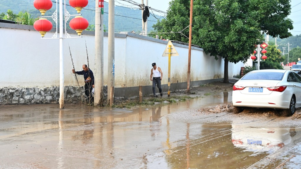 村民在北京平谷一村莊內泥濘的道路旁行走。中新社 村民在北京平谷一村莊內泥濘的道路旁行走。中新社