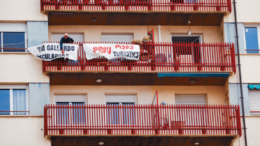 一名男子在公寓外懸掛布條，寫着「不要再有觀光公寓」。（路透社）