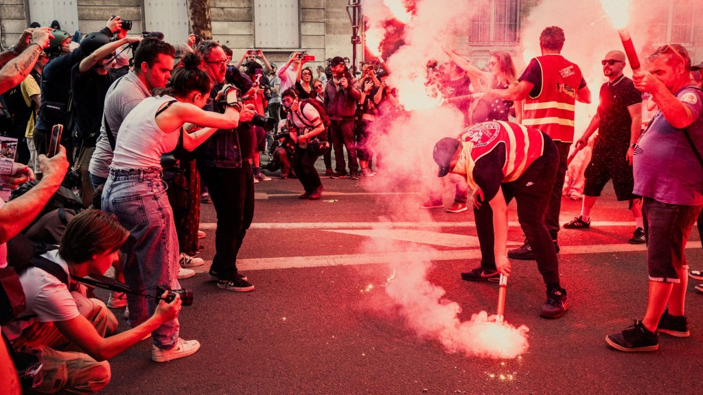 2025年5月1日，人們在法國巴黎的勞動節五一遊行中拍攝手持紅煙的示威者。 法新社
